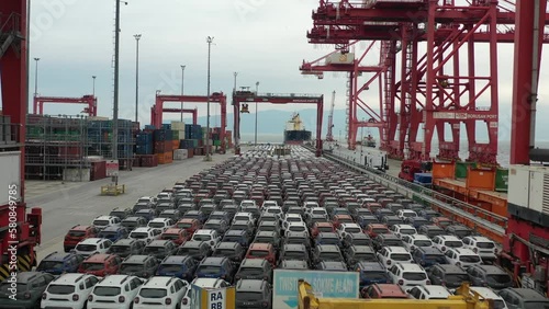 New assorted cars lined up in the port waiting to be loaded on the ro-ro (Roll on Roll off) vehicle car carrier ship. Aerial drone photo. 