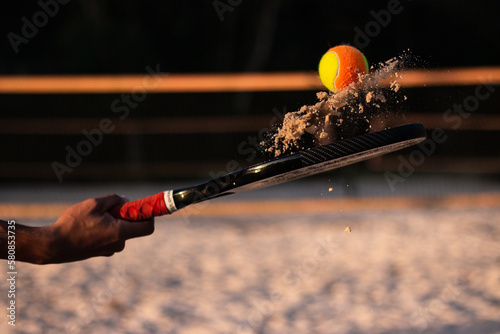 Beach tennis racket and ball. Man holding racket with sand and beach tennis ball on court