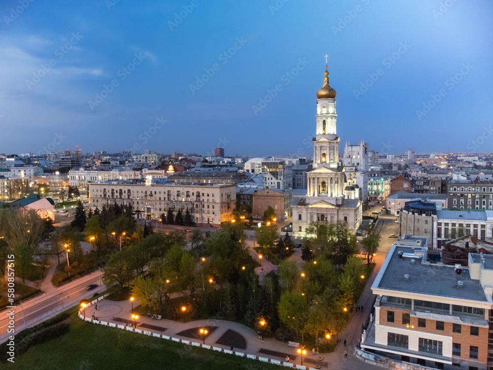 Obraz premium Aerial Dormition Cathedral with golden dome and bell tower on blue sky in evening lights of Kharkiv city downtown, Ukraine.
