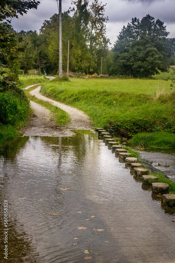 Homemade bridge made of wooden logs across the river. Camino de Santiago. Obstacle in the way. Wooden logs in the water. Nature in rural France. Go to the other shore. Bridge over the river. Homemade bridge made of wooden logs across the river. Camino de Santiago. Obstacle in the way. Wooden logs in the water. Nature in rural France. Go to the other shore. Bridge over the river.
