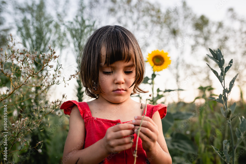 thoughtful girl in red dress watching small sunflower outside thoughtful girl in red dress watching small sunflower outside