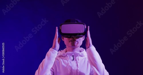 Asian woman using vr headset on blue background, copy space, slow motion photo