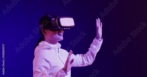 Asian woman using vr headset, touching virtual screen on blue background, slow motion photo