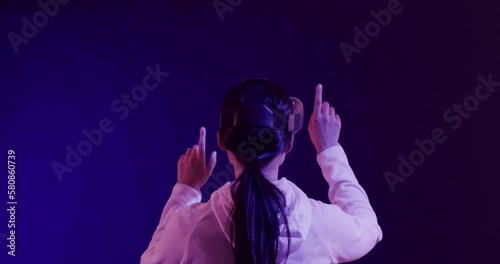 Asian woman using vr headset, touching virtual screen on blue background, slow motion photo