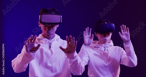 Asian man and woman using vr headsets, touching virtual screen on blue background, slow motion photo