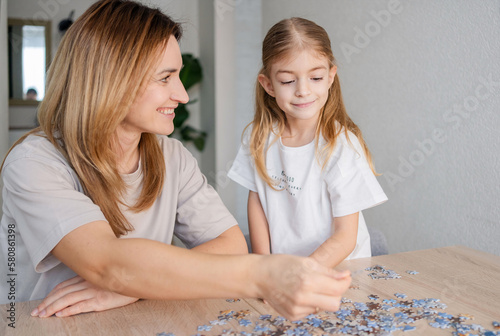 Mother and daughter school age assemble jigsaw puzzle put together pieces playing at home. Leisure hobby having fun. 