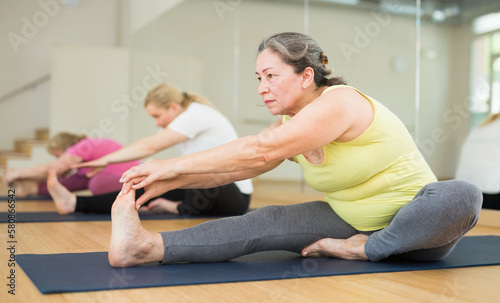 Elderly women practicing yoga, sitting in Seated forward bend exercise, paschimottanasana pose