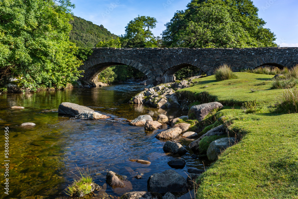 Fototapeta premium The River Duddon flows under the bridge at the picturesque village of Ulpha on the Sella Brow Road in the Lake DistrictNational Park, England.