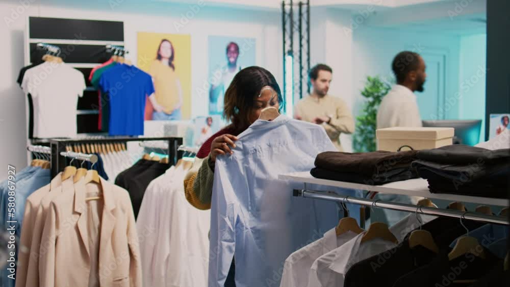 Store customer taking shirt off of hangers to buy clothes, looking at fashion boutique merchandise. Young woman shopping for new trendy collection, examining pants in clothing store. Store customer taking shirt off of hangers to buy clothes, looking at fashion boutique merchandise. Young woman shopping for new trendy collection, examining pants in clothing store.