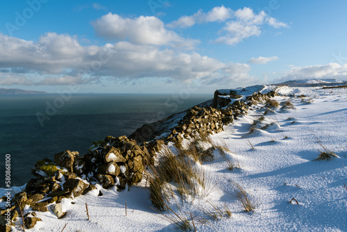 Fotografia Tufts of grass in snow and stone wall above the Irish Sea