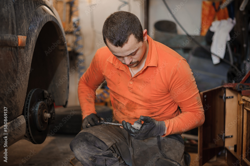 Mechanic man repairs the undercarriage of the car. A man repairs a car in a garage. Car wheel repair