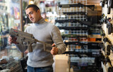 Caucasian man choosing machine gun in airsoft shop.