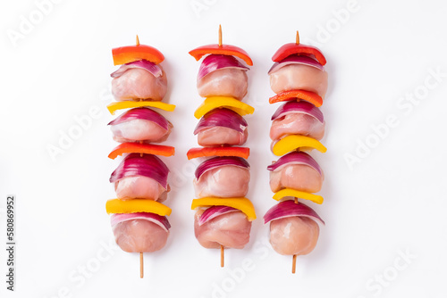 Skewers with pieces of raw meat, red, yellow and green pepper.Top view.Uncooked mixed meat skewer with peppers.Raw chicken leg meat skewers with vegetables, peppers, onions, on a white background.