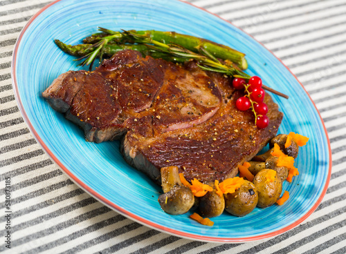 Roasted veal steak with seasonings served with baked vegetables and rosemary on striped textile surface