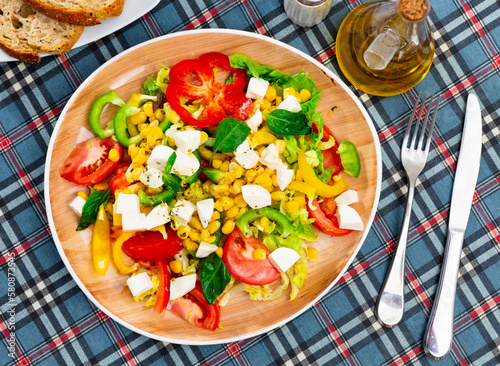 Vegetable salad with colorful bell pepper, tomatoes, corn, napa cabbage and soft cheese, decorated with fresh basil leaves