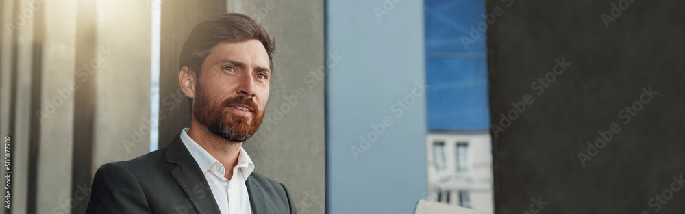 Focused Businessman working on laptop outside office building and looking away Focused Businessman working on laptop outside office building and looking away