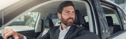 Handsome businessman in grey suit is riding behind steering wheel of car © Kostiantyn