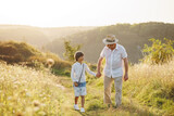 Photo of a little boy with his grandfather walking in a field at summer