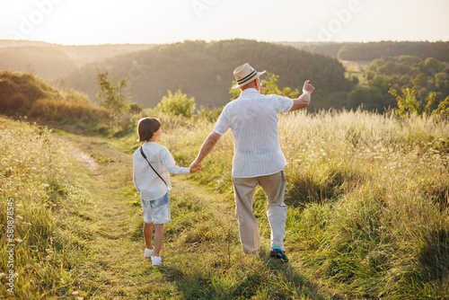 Backside photo of a little boy with his grandfather walking in a field at summer