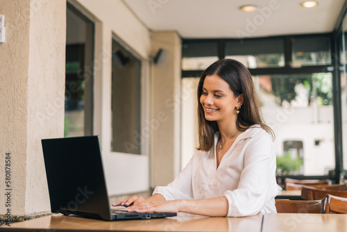 A beautiful Caucasian student is studying at a distance learning university. She is sitting at a table at home with a laptop and a notepad