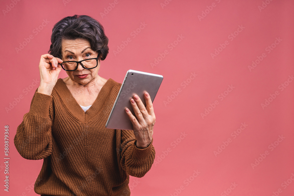 Portrait of senior aged mature woman with tablet computer, grandmother isolated on pink background. Portrait of senior aged mature woman with tablet computer, grandmother isolated on pink background.