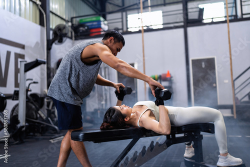 Male fitness center instructor help woman lifting dumbbell workout at fitness center