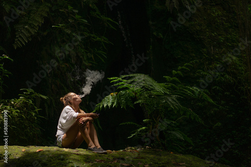 Young woman smokes a vape in the jungle on a tropical island, Bali. photo