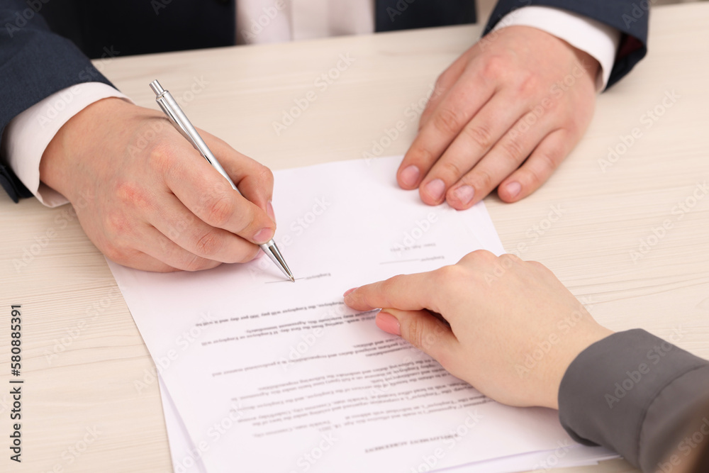Woman pointing at document and man putting signature at wooden table, closeup Woman pointing at document and man putting signature at wooden table, closeup