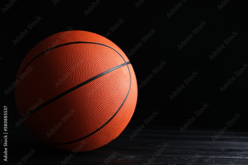 Obraz premium Basketball ball on black wooden table against dark background, space for text