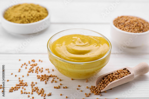 Bowl with delicious mustard and seeds on white wooden table
