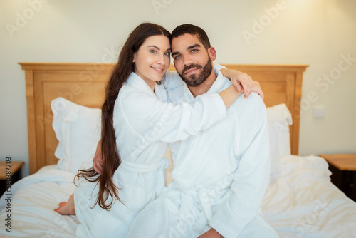 Happy Diverse Spouses Embracing Sitting On Bed Indoors