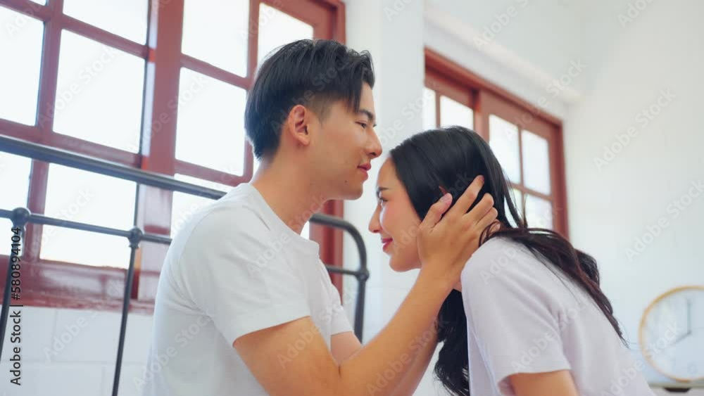 Asian husband kissing his wife while sitting on bed in bedroom at home. Asian husband kissing his wife while sitting on bed in bedroom at home.