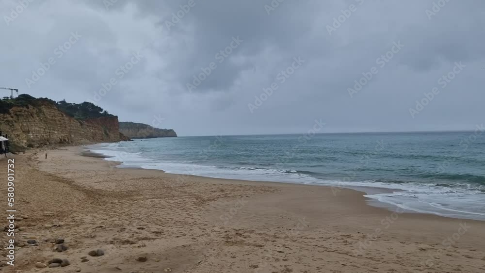 The shot is made at Praia Dona Ana, 8600-500 Lagos, Portugal in March on a cloudy, rainy day facing the sea with rock formations, and the beach in the shot. The shot is made at Praia Dona Ana, 8600-500 Lagos, Portugal in March on a cloudy, rainy day facing the sea with rock formations, and the beach in the shot.