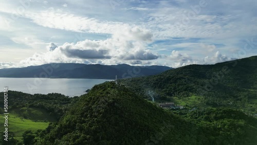 Rotating Aerial View of lush jungle-covered mountain amidst province of Catanduanes with small barangay town and idyllic ocean bay in the background. photo