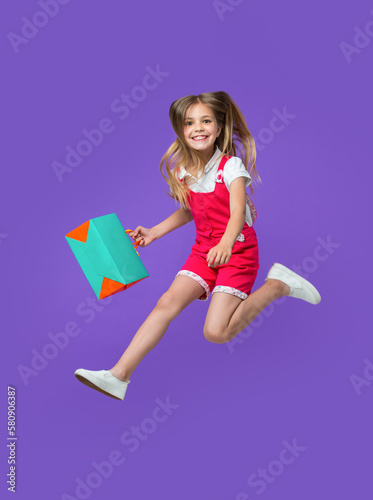 cheerful teen girl jumping after shopping isolated on purple. teen girl jumping after shopping