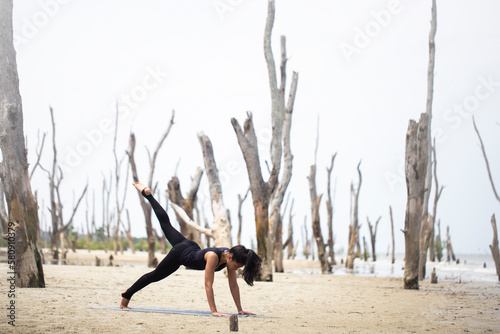 young asian woman practicing yoga on the beach