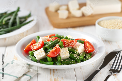 Fresh summer green beans salad bowl with tomatoes, feta, and sesame. Plate with delicious green beans salad on wooden table, closeup
