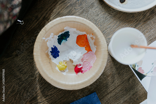 A paper bowl with small batches of vivid colors like yellow, blue, orange, red and pink in an arts and crafts environment