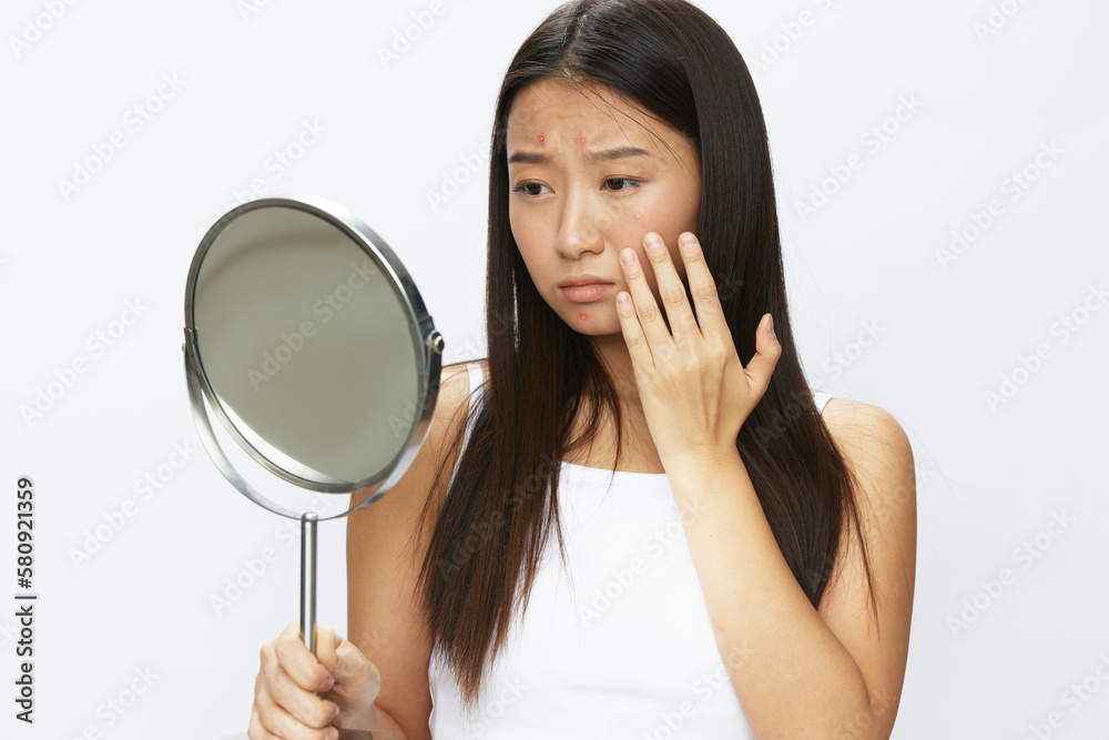 Asian woman with mirror in hand facial skin problems, acne and inflammation, red rash and allergies, chicken pox, sadness from rashes. Facial skin care concept for diseases and nerves Asian woman with mirror in hand facial skin problems, acne and inflammation, red rash and allergies, chicken pox, sadness from rashes. Facial skin care concept for diseases and nerves