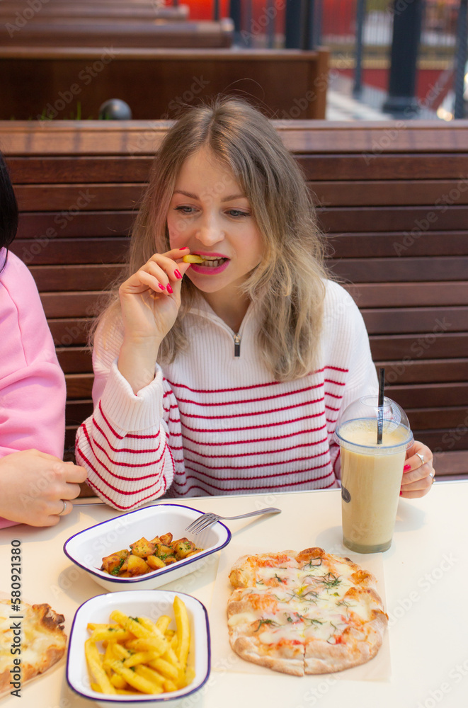 Beautiful blonde woman eating french fries in cafe with friend Beautiful blonde woman eating french fries in cafe with friend