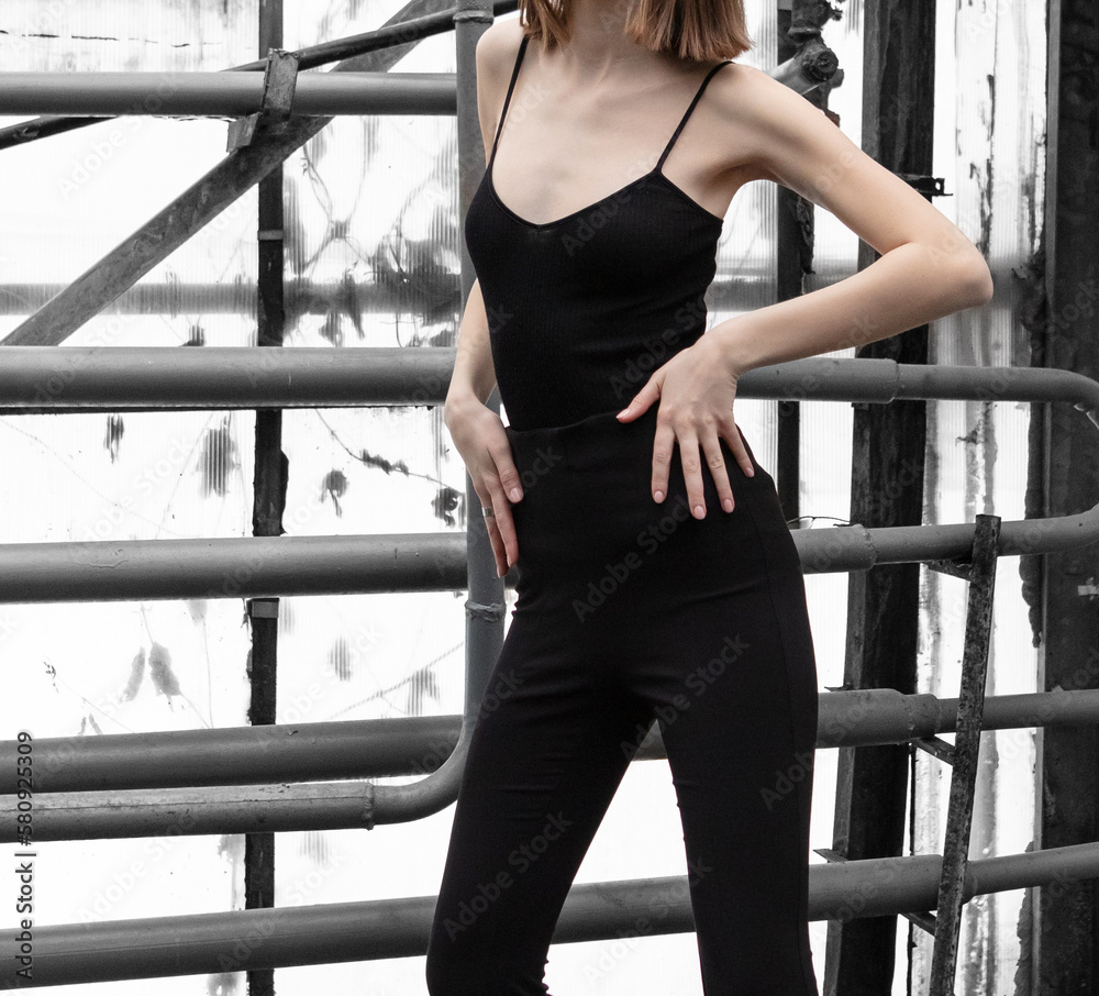 A girl in black clothes poses near metal pipes. A girl in black clothes poses near metal pipes.