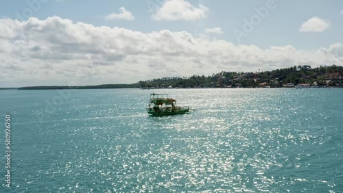 Rotating aerial drone shot following a small transport boat sailing on a tropical turquoise river from the Restinga beach to the Barra do Cunhaú beach in Rio Grande do Norte, Brazil photo