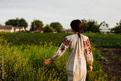 A girl in a national costume in a field against a background of green trees and bushes