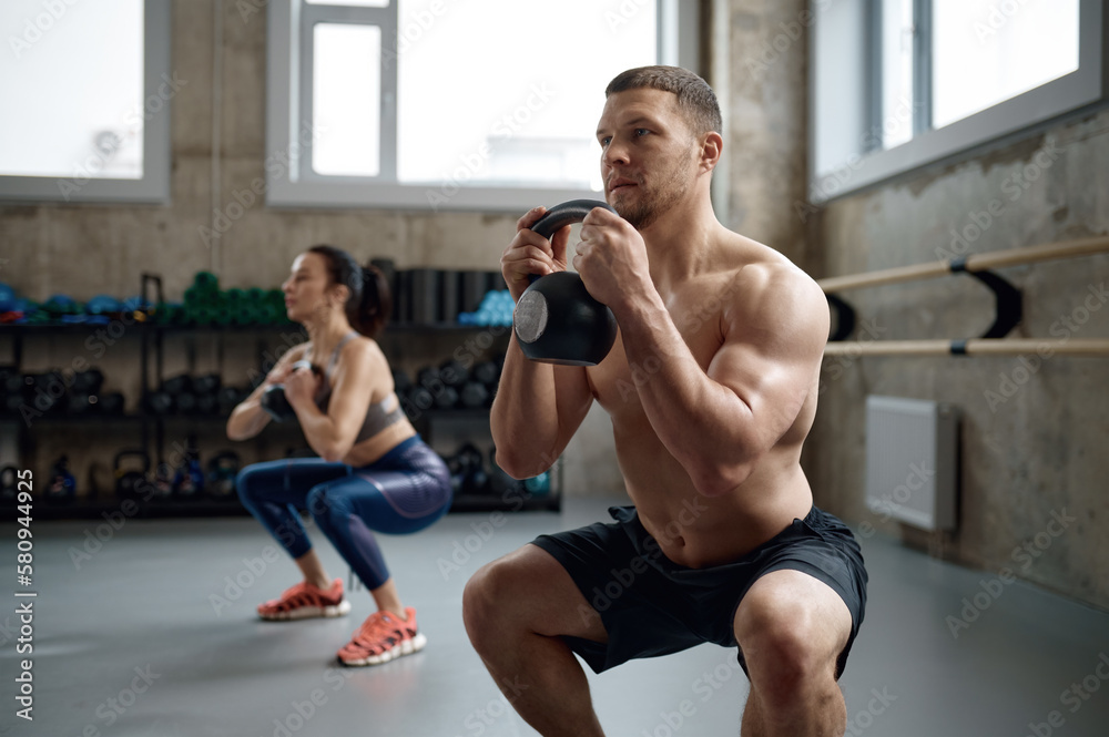 Man and woman with good physique holding heavy kettle bell Man and woman with good physique holding heavy kettle bell