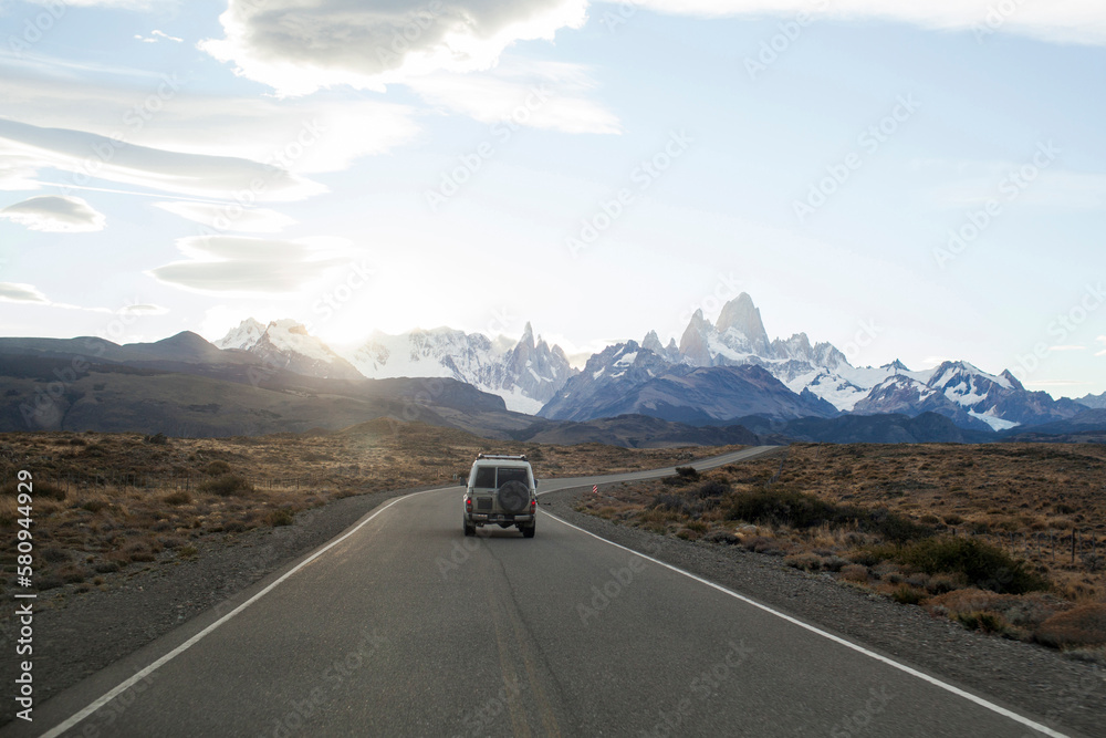 Off-road vehicle moving on road leading towards mountains Off-road vehicle moving on road leading towards mountains