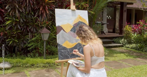 Creative young female artist painting a picture with acrylic paints outdoors. Creativity, hobby and art concept