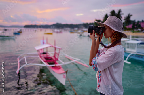 Photography and travel. Young woman in hat holding camera with beautiful tropical sea view.