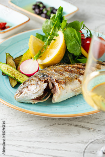 Grilled sea bream with vegetables and greens on wooden table