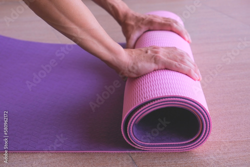 Yoga rug in the hands of a man on a floor, close up of man spreads purple pink fitness mat for starting training