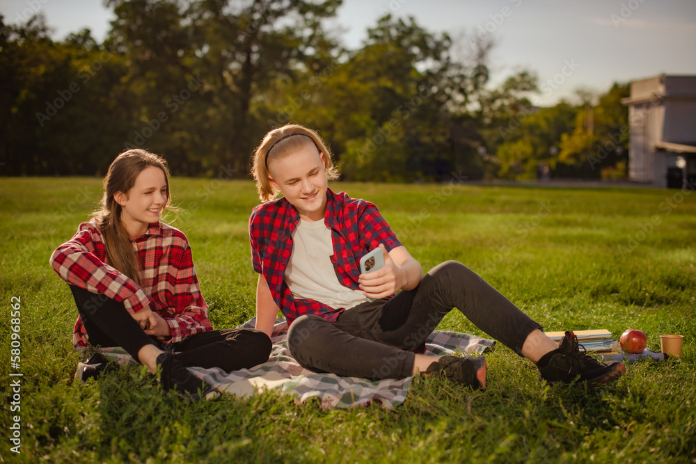 teenagers girl and boy watching video on smartphone on green grass in school yard teenagers girl and boy watching video on smartphone on green grass in school yard